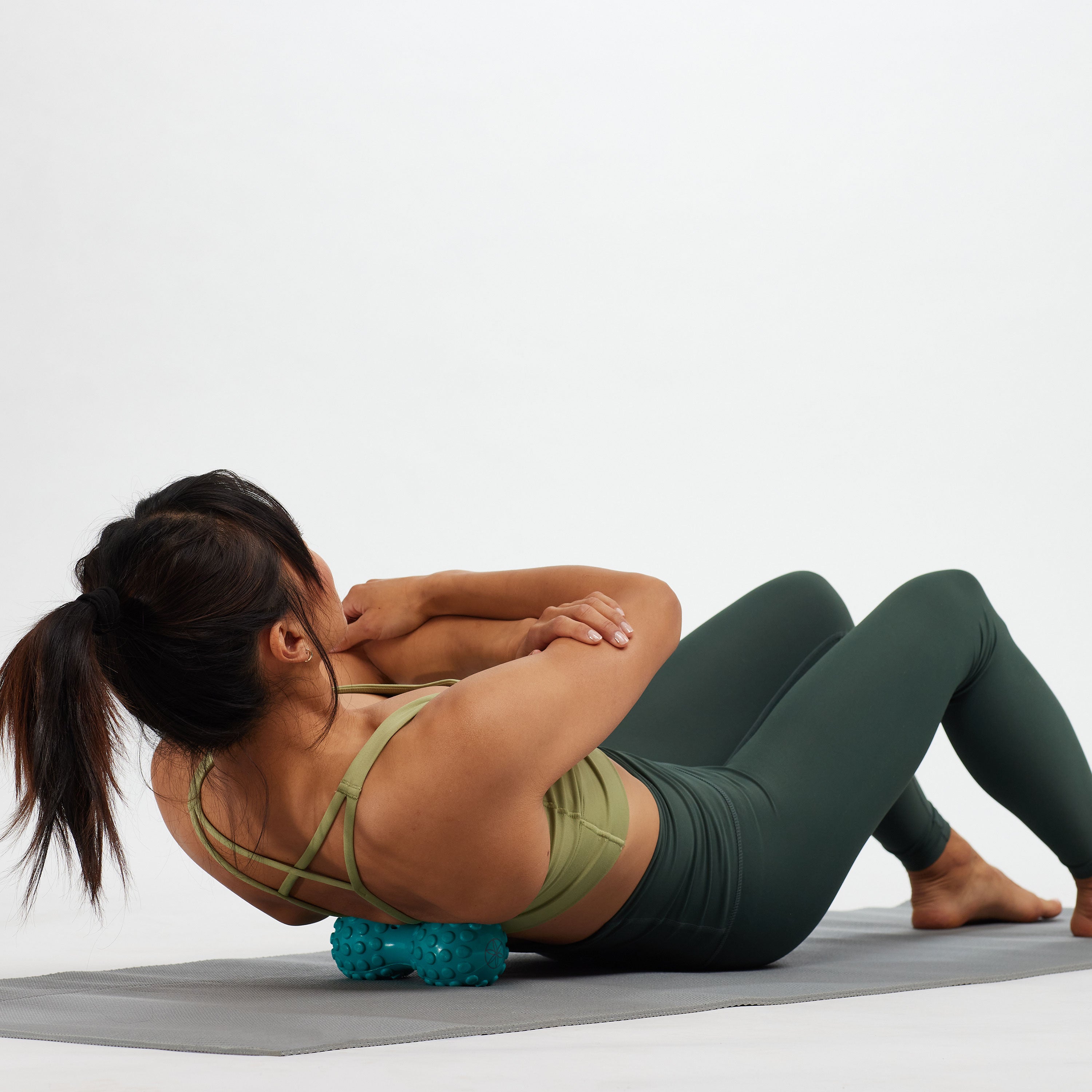 Person on a yoga mat with the Restore Dual Zone Back Roller  under the upper back near the shoulders.